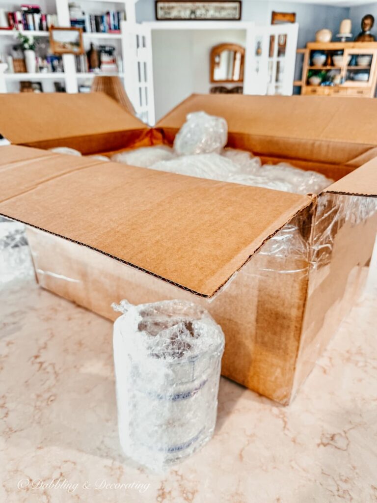 Large box filled with bubble wrapped vintage finds from a weekend antiquing in Maryland on kitchen counter.