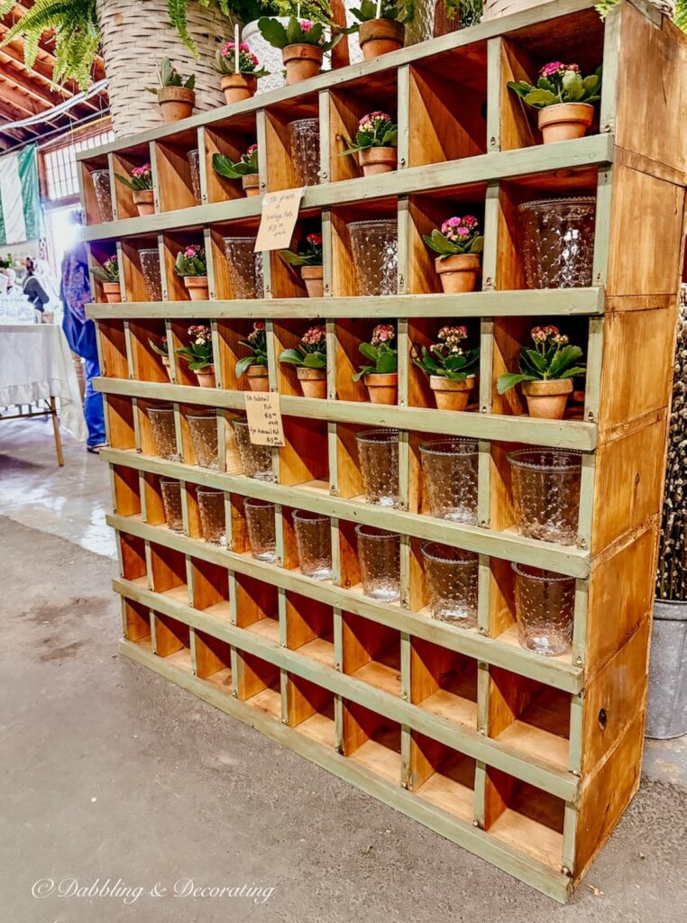Large wood cabinet with cubby holes filled with terracotta pots and pink flowers in vintage booth at Vintage Market Days.