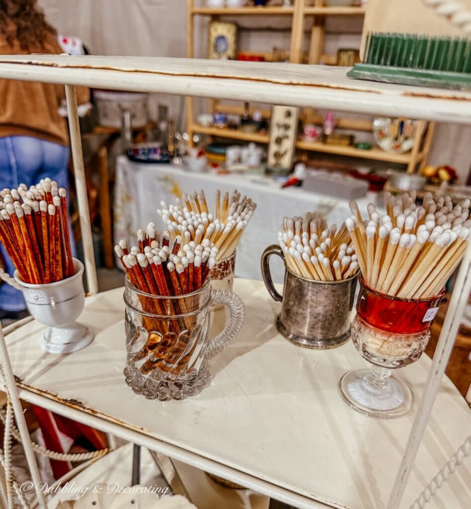 Match collection displayed in vintage booth in glass, silver, colored glass, and ironstone small mugs.