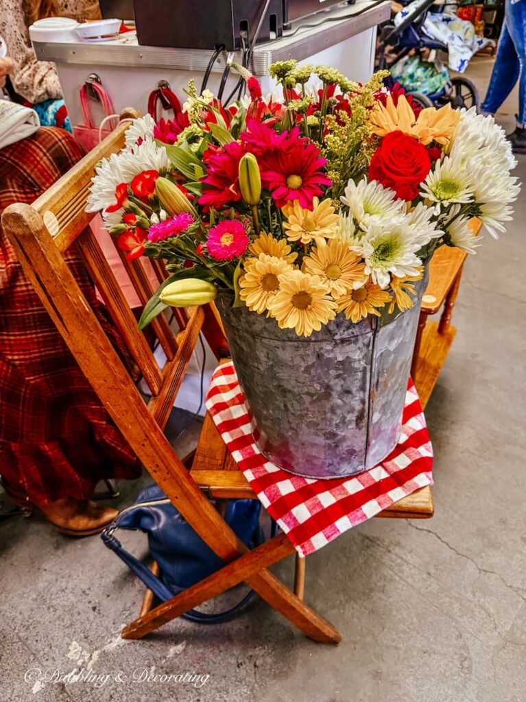 Galvanized bucket filled with spring flowers in vintage booth on chair at Vintage Market Days.