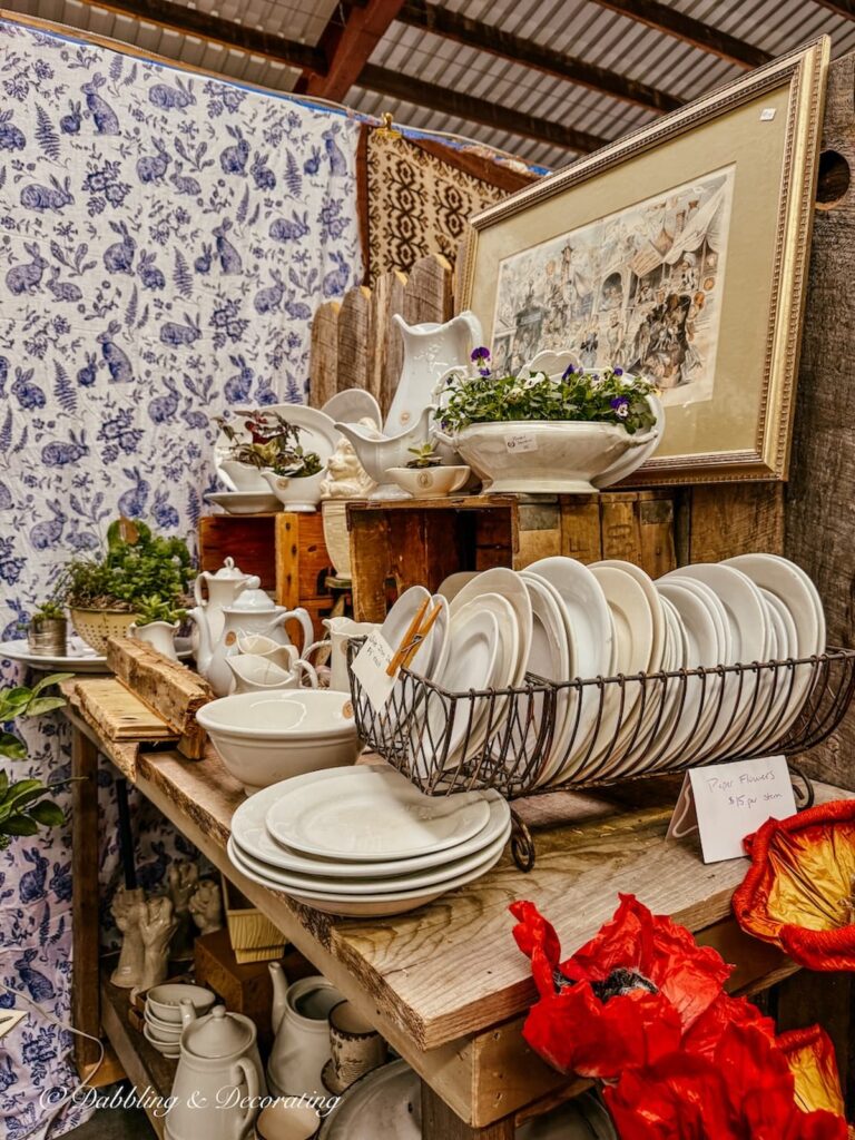 Vintage booth styling ideas with dish racks filled with ironstone plates and stacked white pitchers and layered details.