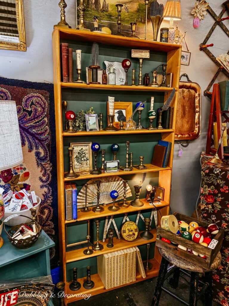 Tall wooden bookcase decorated with vintage brass candlesticks, pool balls and green accents in a vintage booth.