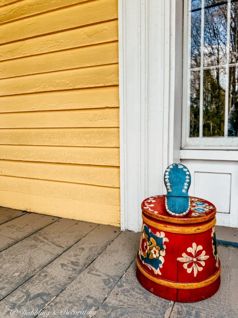 Yellow farmhouse porch with a vintage German shoe shine box in bright red with blue and Scandinavian designs.