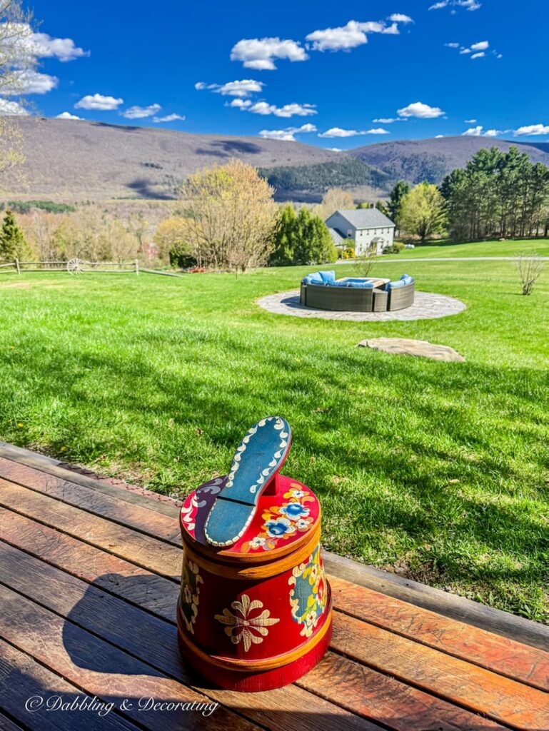 Vintage German shoe shine box in decorative nordic style reds, blues, yellow prints on porch at home in the Vermont mountains with a view.