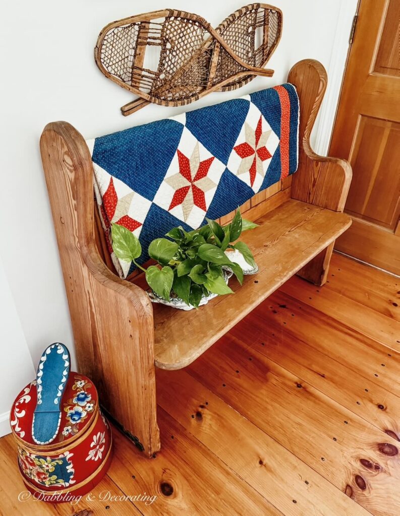 Vintage church pew in entryway with blue quilt, snowshoes on wall and colorful vintage German shoe shine box.