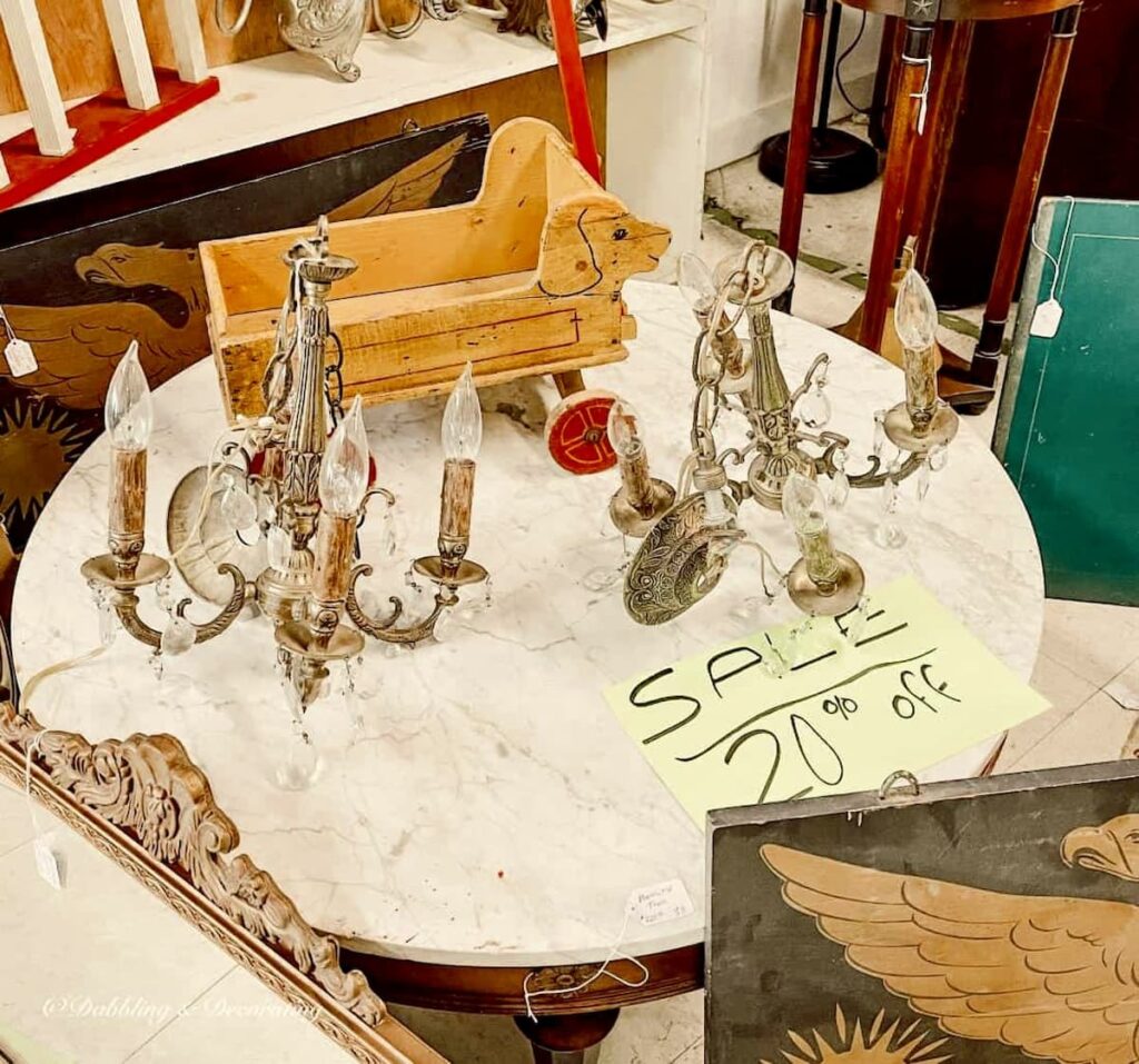 Two vintage small small chandeliers on marble table with 20% off sign on thrift store table.