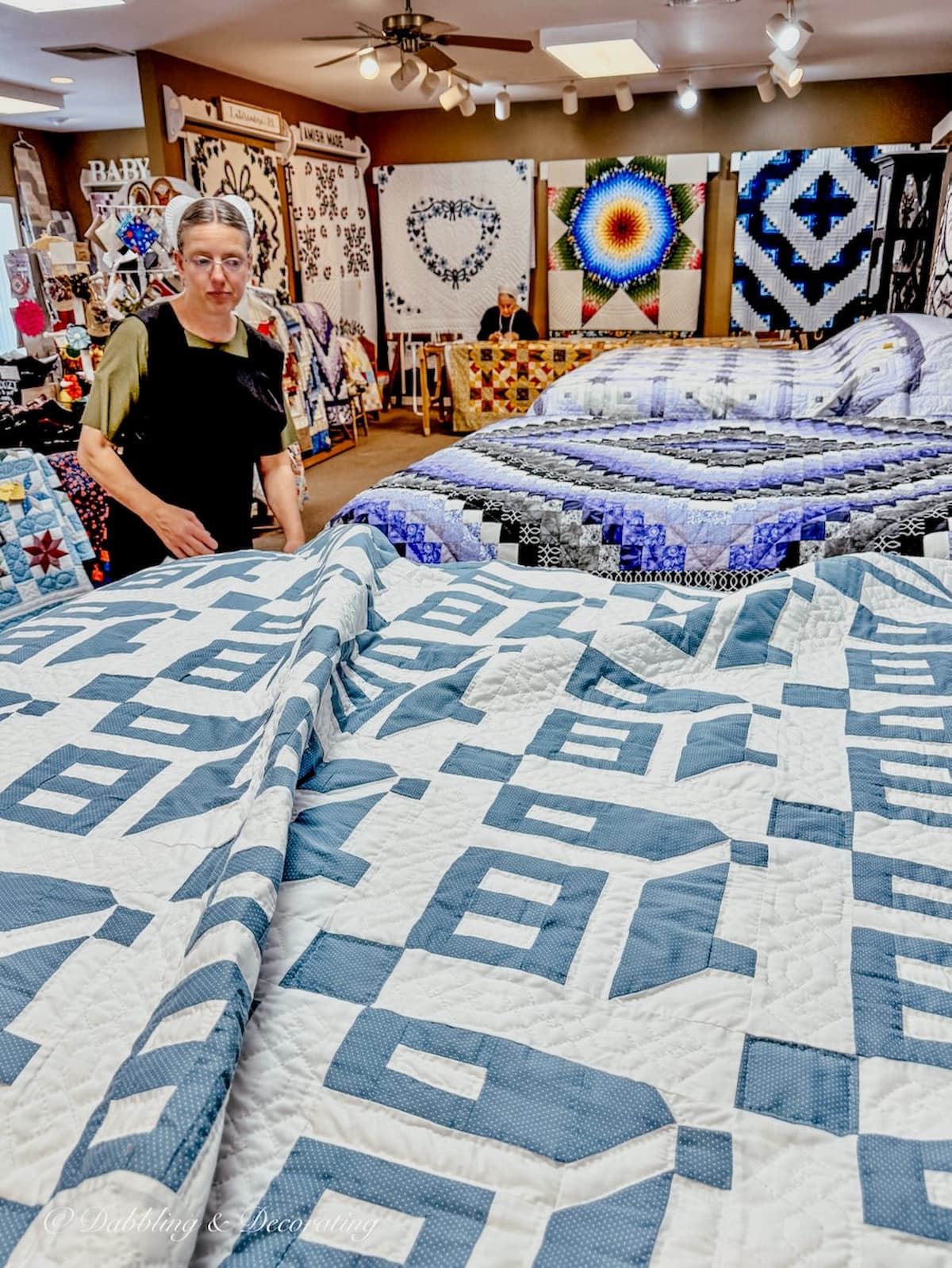 A blue and white Amish quilt laid out in a shop in Lancaster, PA with an Amish woman sharing it's history and story.