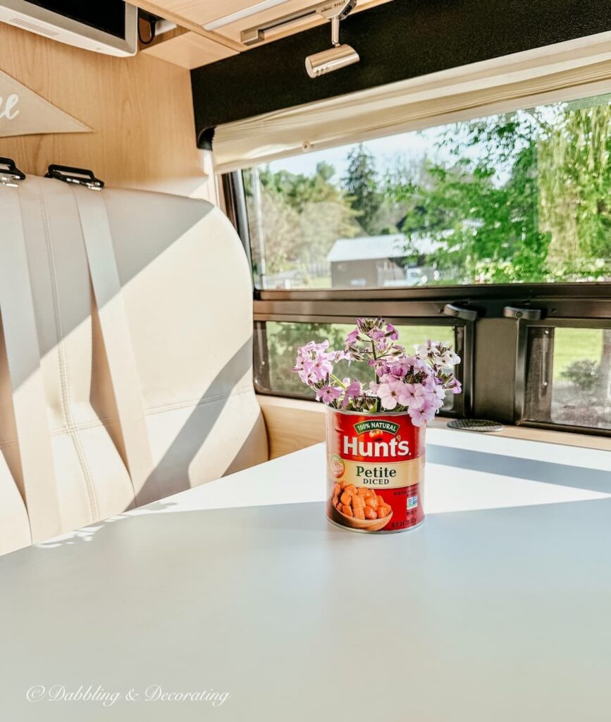 Inside an RV with a sitting area with table and a spaghetti can filled with wildflowers.
