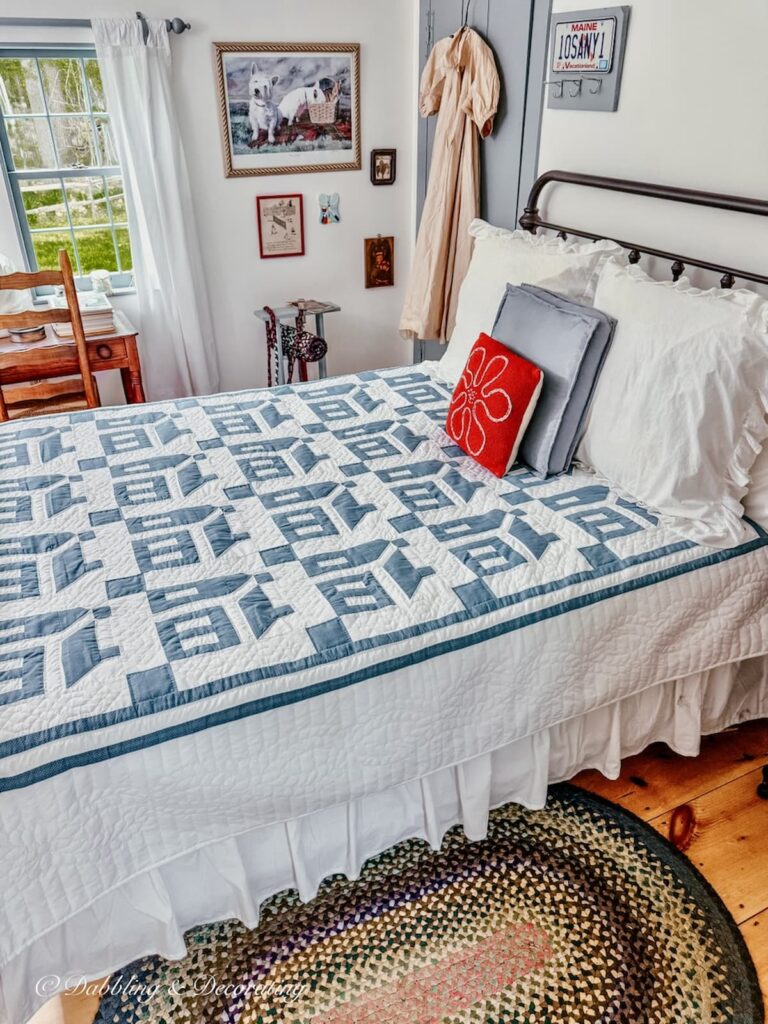 Blue and white Amish quilt displayed on small guest bedroom wrought iron bed with braided rug.