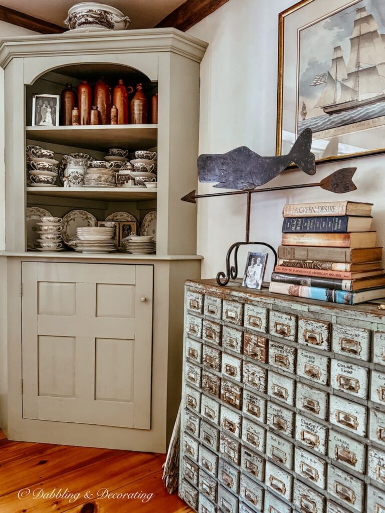 Vintage built-in corner hutch filled with brown and white transferware and a collection of brown jugs next to a dining room apothecary cabinet.