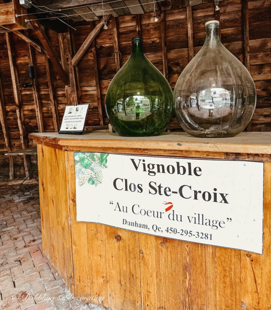 Green and white large demijohn bottles for sale on wooden serving table at the VIGNOBLE CLOS STE-CROIX in Dunham, Quebec.