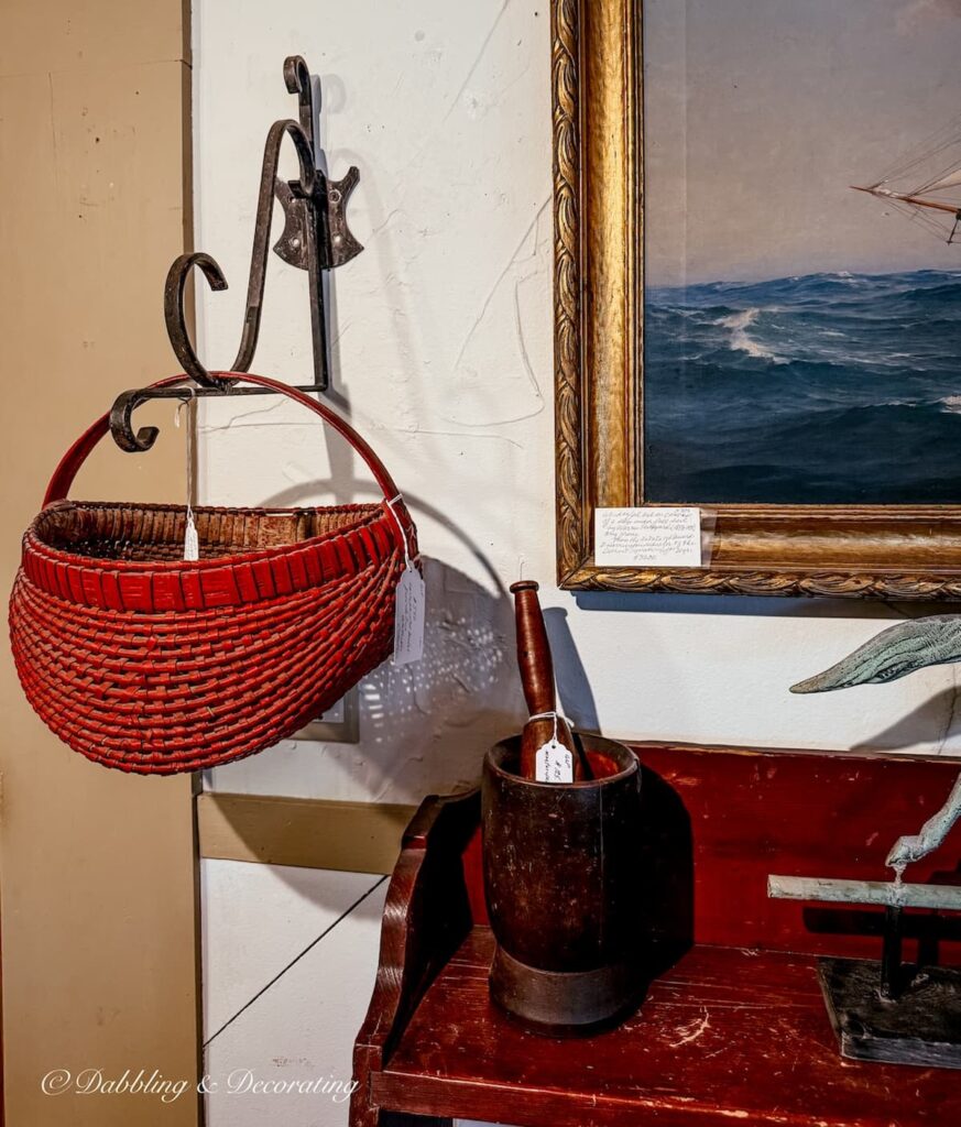 Primitive red basket hanging from a wrought iron antique hook in an antique store for the perfect heritage Americana decor detail.