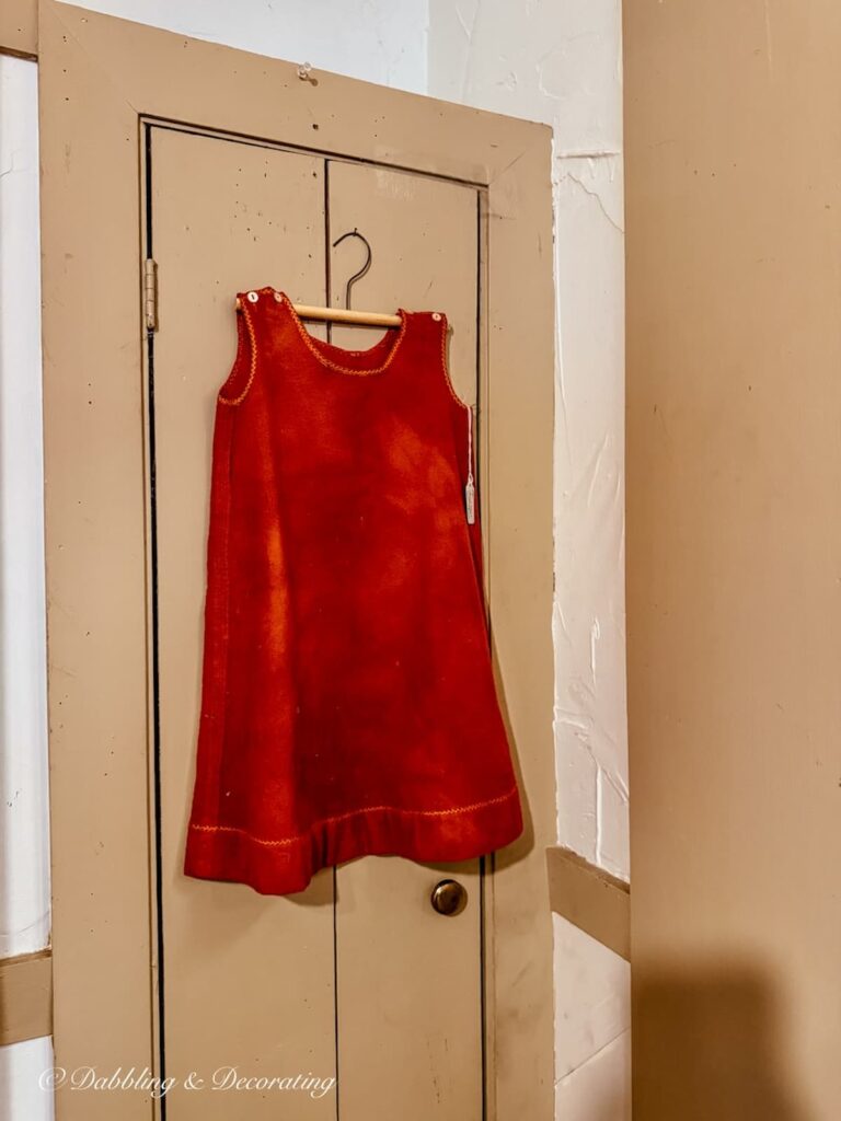 Child's red antique dress hanging on a primitive latched door inside a New England antique shop.