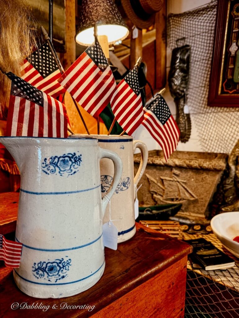 Two vintage stoneware pitchers with blue accents and American flags displayed inside them at the York Antique Gallery in Maine.  Heritage Americana Decor