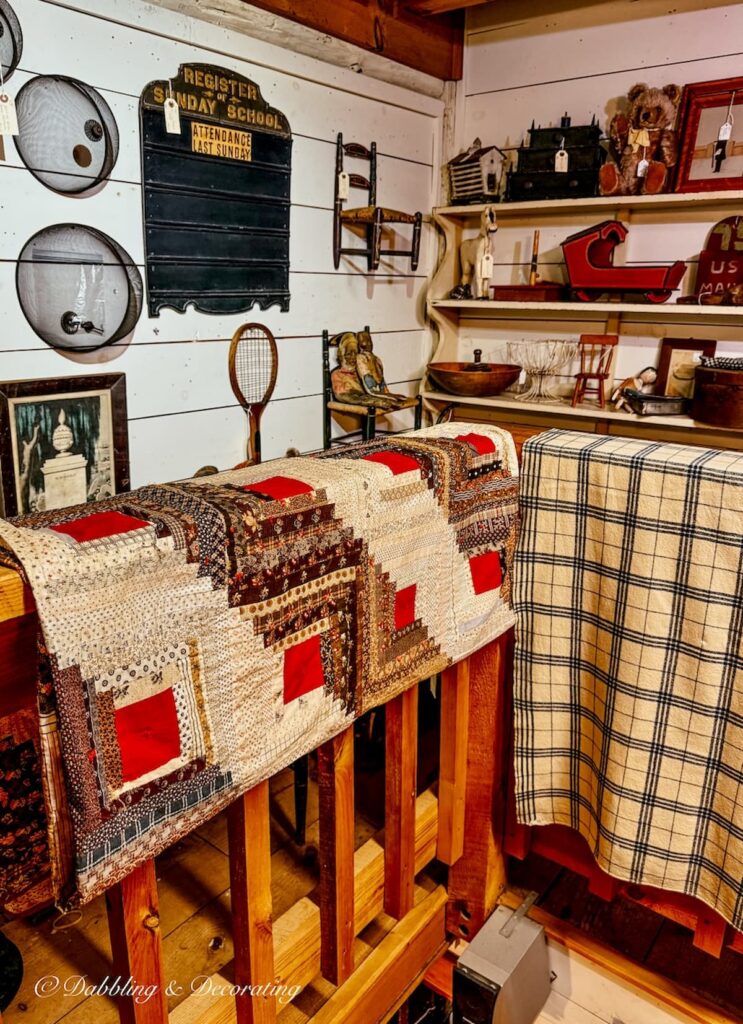 Antique quilt with brown and red muted coloring hanging on stairway railing in New England antique store. Heritage Americana Decor