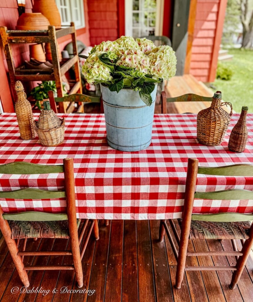 Vintage blue ice cream bucket with hydrangeas on red gingham tablecloth on covered front porch flower pot ideas.