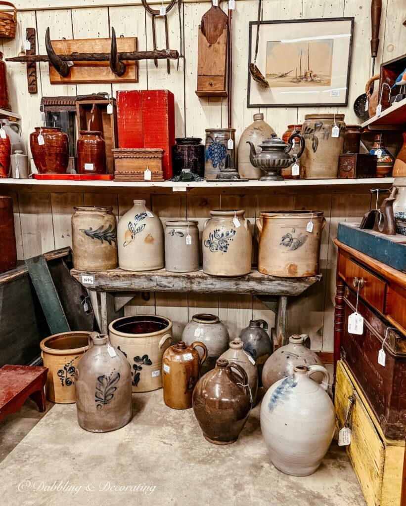 Vintage booth at antique store filled with antique crocks blue embossed motifs in all different shapes and sizes for Americana decor ideas.