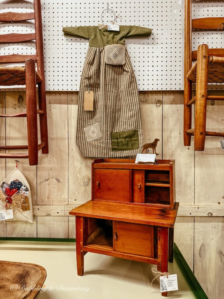 Decorative primitive child's dress hanging on the wall of a vintage booth inside a Vermont antique store.