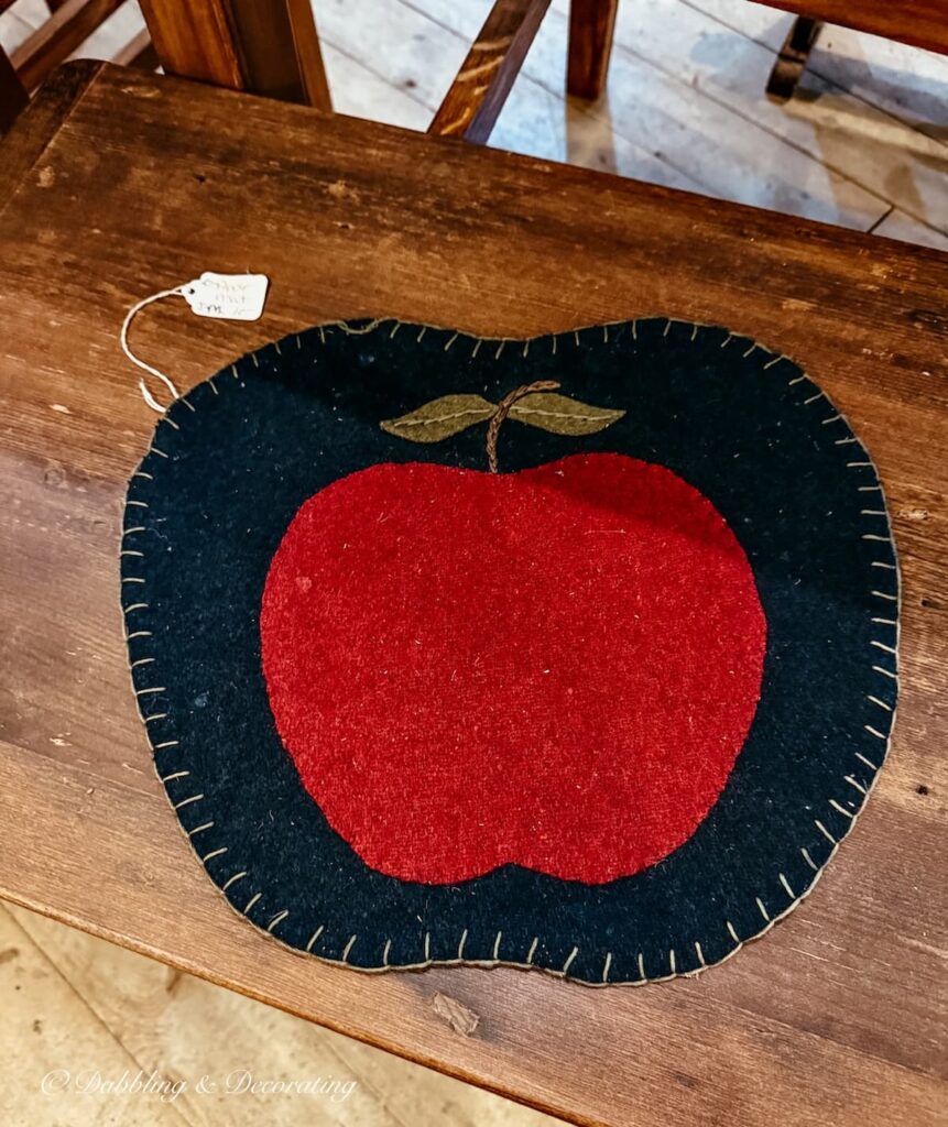 Felt chair pad in black with a red apple on wooden bench in antique store.