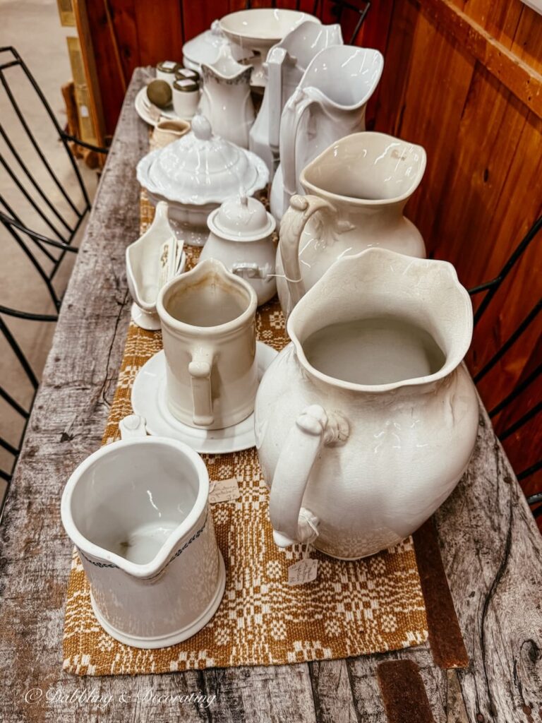 A collection of white ironstone pitchers on a farmhouse table in a Vermont antique store.
