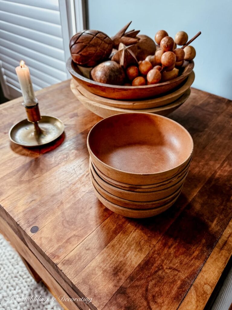 Vintage wooden bowls stacked on top of a vintage butcher clock with a small lit brass candlestick and white taper.