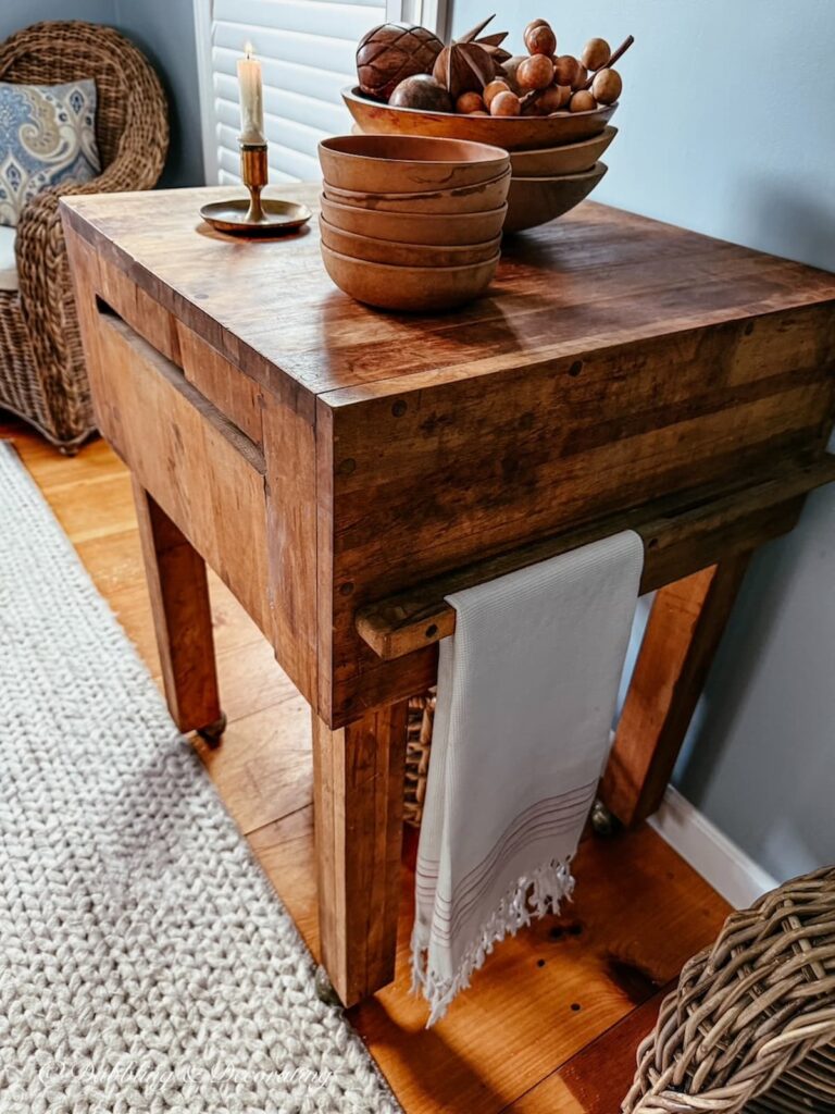 Antique butcher block table styled with wooden bowls and one simple small brass candlestick and lit white taper in scullery corner.