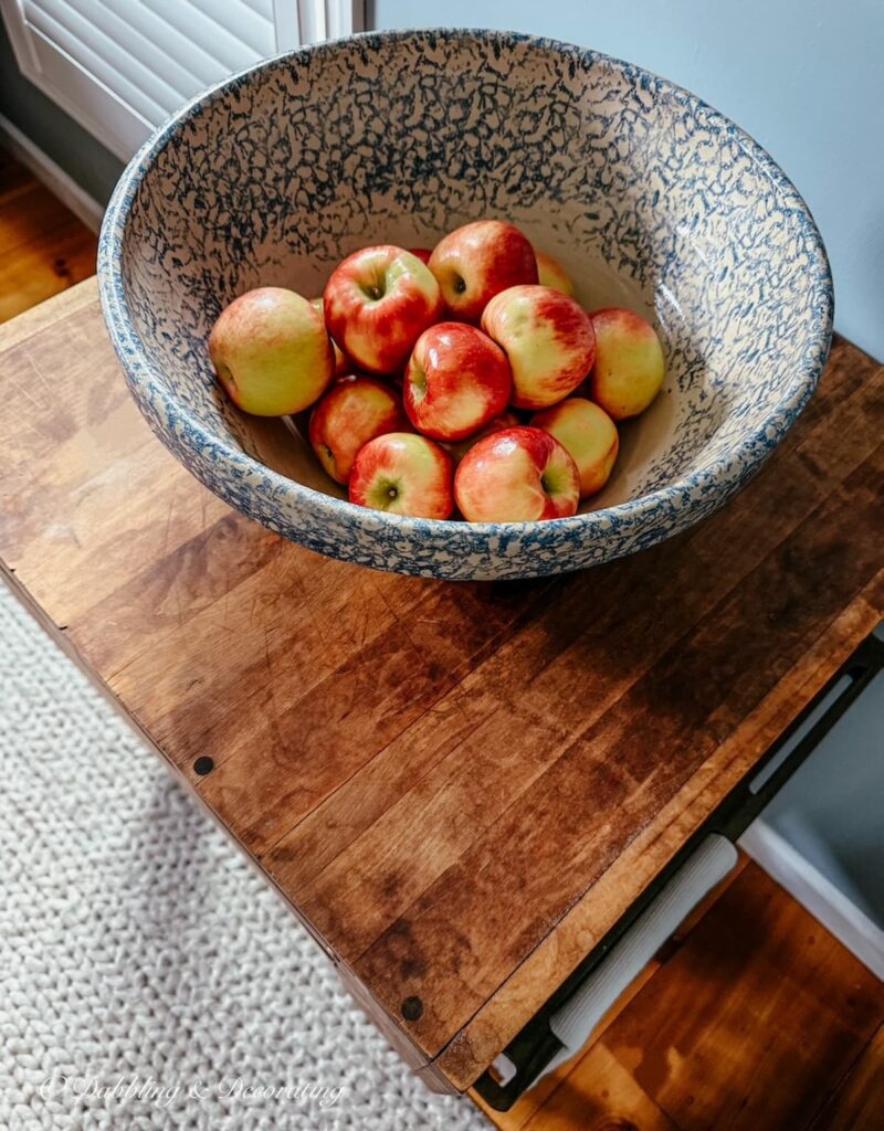 Blue and white large spongeware bowl filled with apples on top of an antique butcher block island.