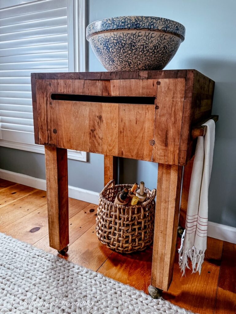 Large antique butcher block table with blue and white vintage spongeware bowl on top, a basket of vintage rolling pins underneath and a French tea towel hanging off it's side.