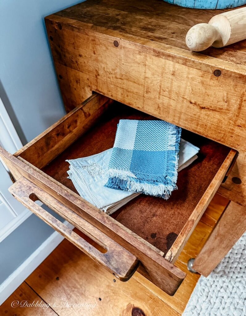 Wooden drawer on vintage butcher block table with blue and white vintage napkins collected inside.
