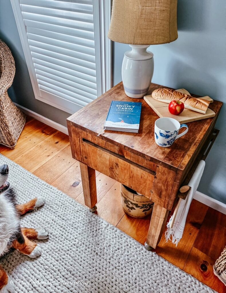 Vintage butcher block styled with a thrifted lamp, open cookbook breadboard with French Bread and an apple in kitchen scullery with Bernese Mountain Dog looking on.