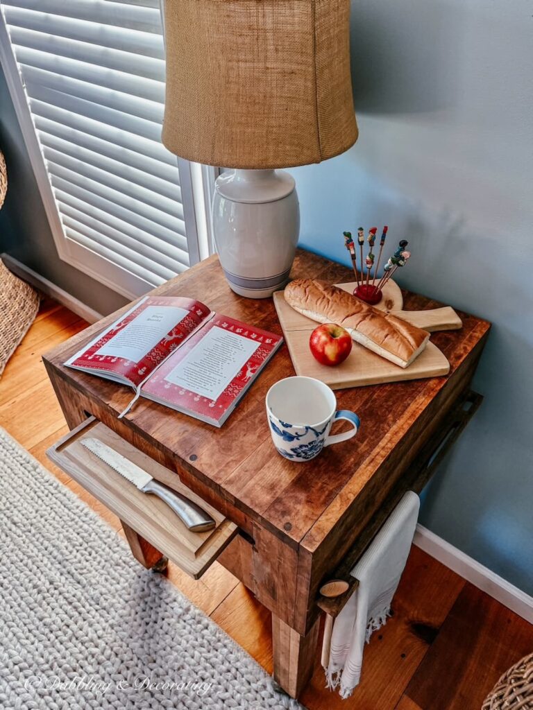 Vintage butcher block table displayed in kitchen scullery with open recipe book, breadboard and cozy lamp.
