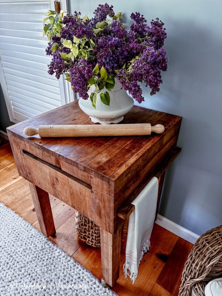 Vintage wooden butcher block table displayed with a lilac arrangement and an oversized wooden rolling pin in unfitted kitchen scullery.
