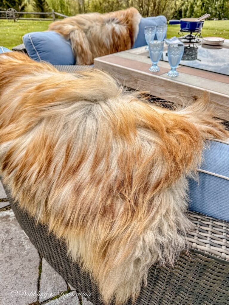 Rare Sheepskins in foxy British color draped over backyard fire pit sectional seating with blue cushions. Are Sheepskins worth it? You betcha!