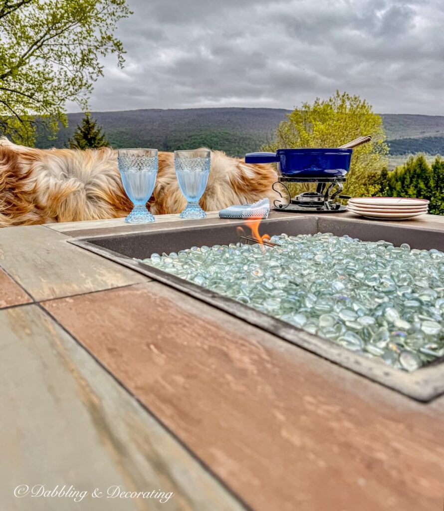 Backyard gas fire pit with mountain views, a fondue set and brown sheepskins draped on sectional seating around the fire pit.