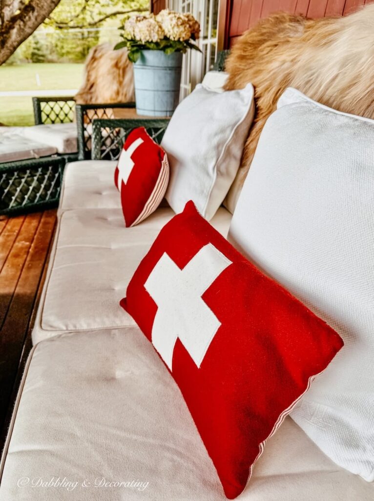 Rare Sheepskins in tan, whites, and grays draped over a covered porch sofa with red cross pillows at home in Vermont.