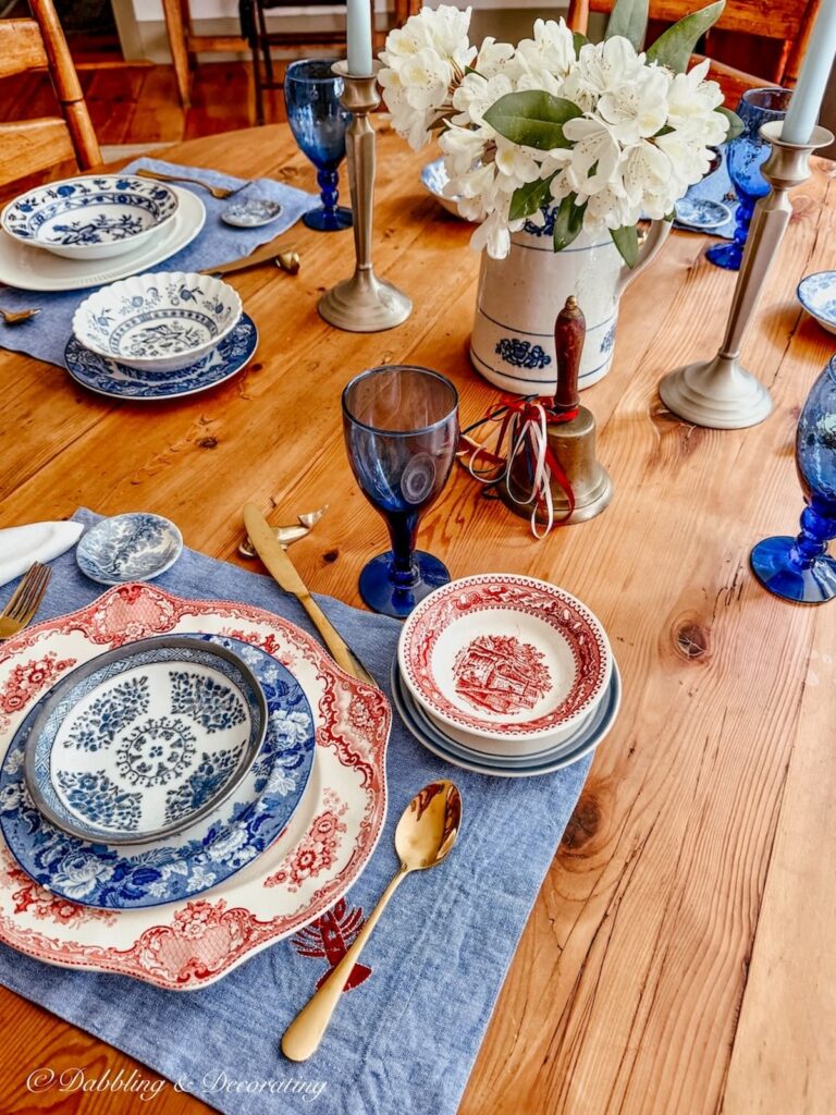Vintage red, white and blue place settings on a round antique wooden table with mix and max vintage dishes collected over time.