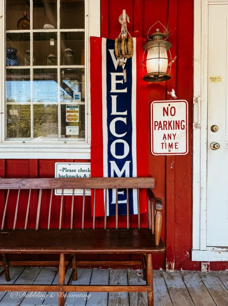 Welcome sign on red bar at the Wiscasset Antique Mall in Maine with welcome bench on porch.
