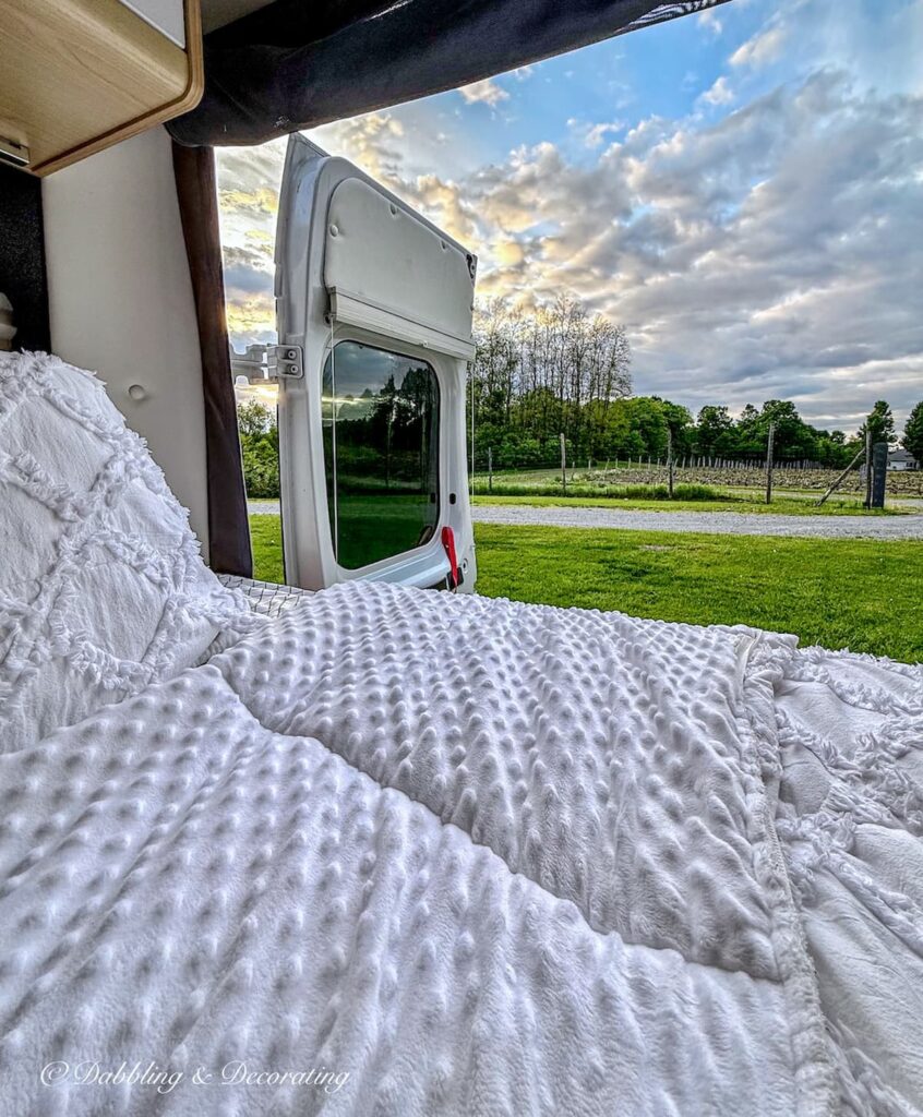 Back of traveling RV with open door and bed looking out at the VIGNOBLE CLOS STE-CROIX in Dunham, Quebec at sunset.
