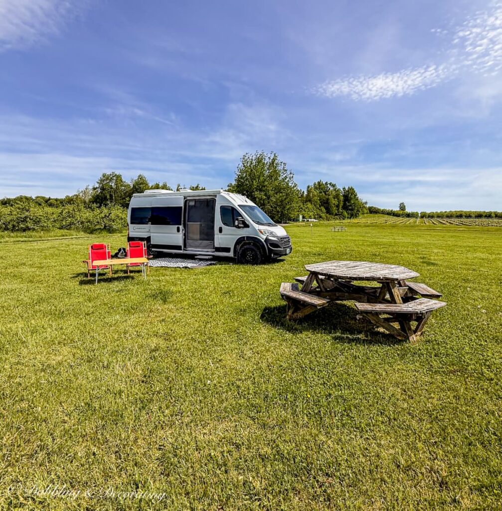 White Class B Panoramic RV on top of hill with red chairs and rustic picnic table at Vignoble de l'Orpailleur in Dunham, Quebec.