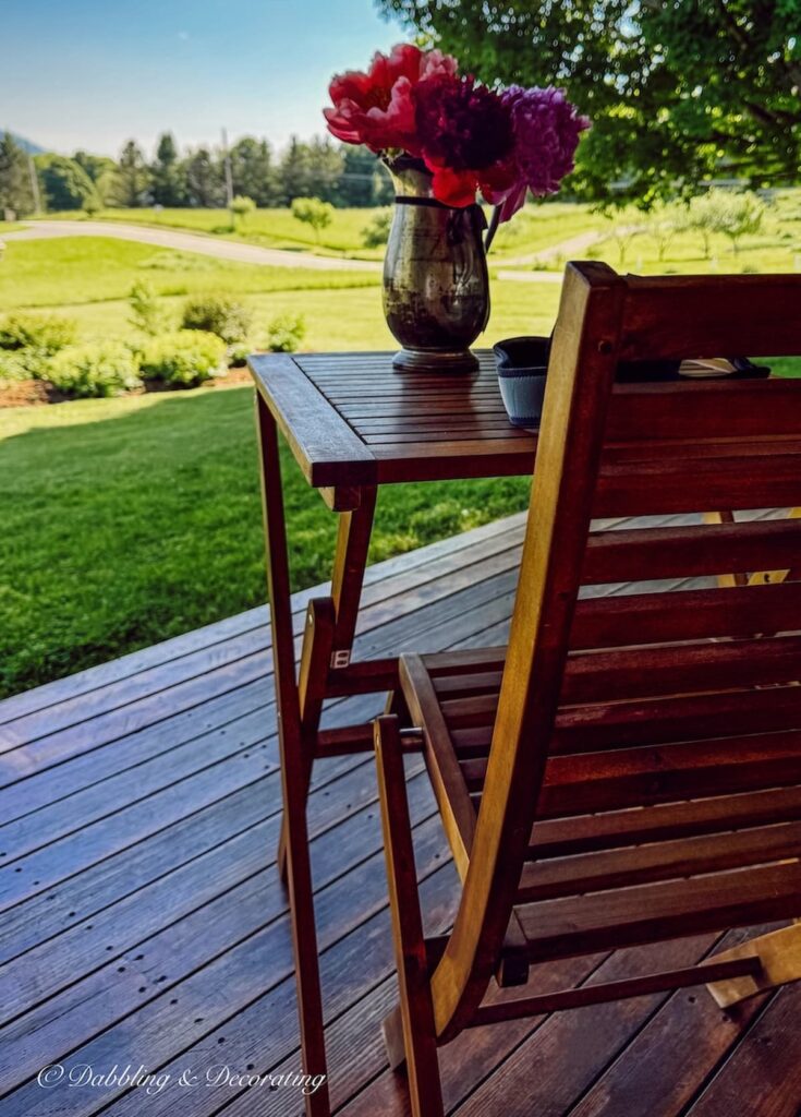 Bistro table in teak with chair a table for one with peonies in a silver pitcher on covered porch in Vermont.