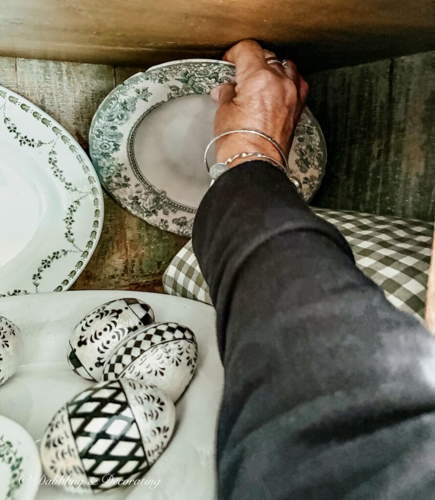 Arm reaching into an antique cupboard and grabbing an antique green and white transferware bowl.
