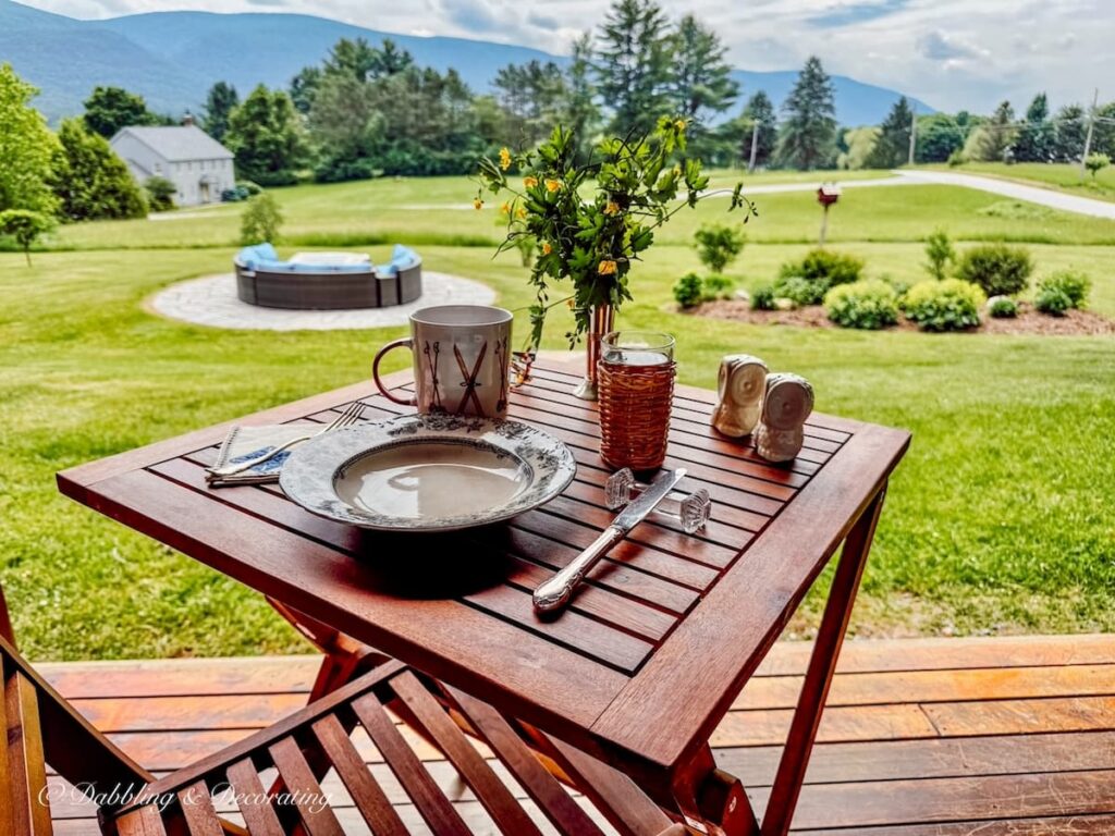 Breakfast table set for one with bistro teak table on covered porch with mountain views in Vermont.