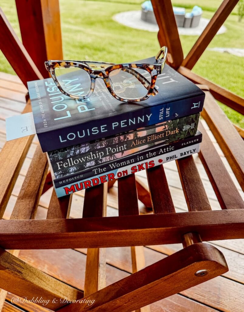 A stack of summer reading (books) on bistro chair with a pair of reading glasses.