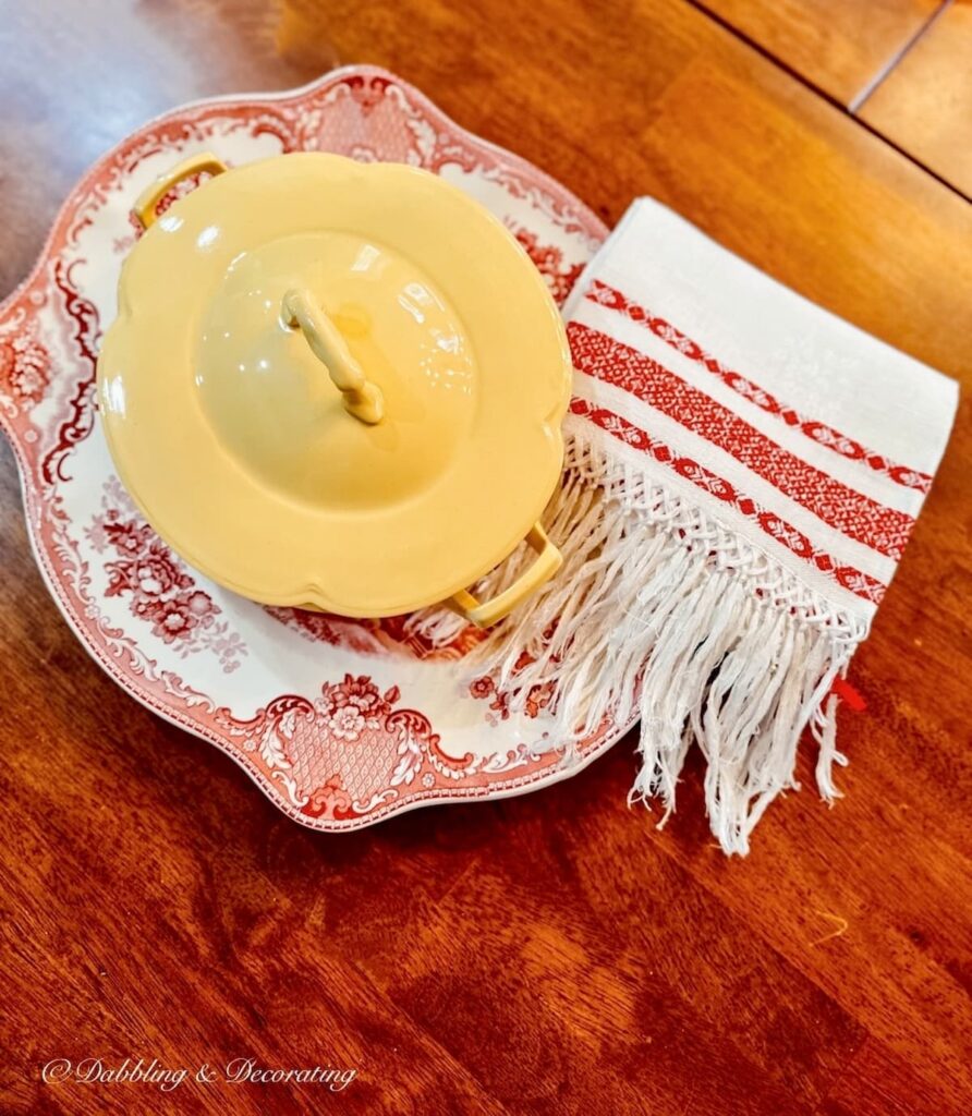 Thrifted yellow soup tureen layered with red transferware platter and red and white tea towel at an Estate Sale.