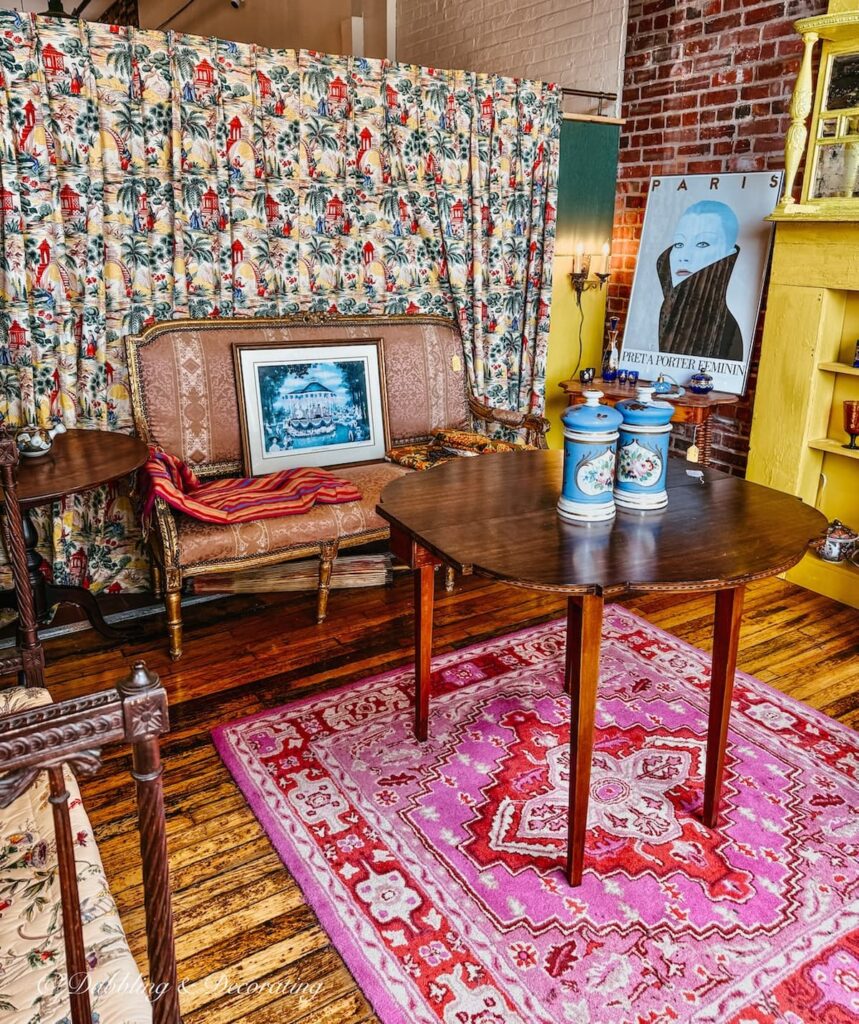 Colorful mid century modern styled booth display with pink rug, blue glassware, draped wall covering and yellow bookshelves at Portland Antiques Mall in Maine.