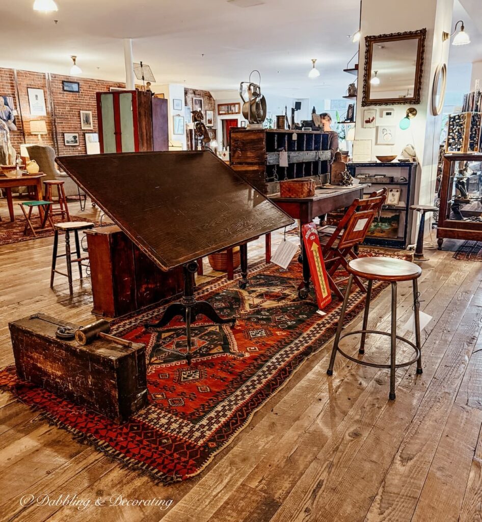 Antique wooden large drafting table on red antique rug displayed with drafting stool and more at Open House Portland, Maine.