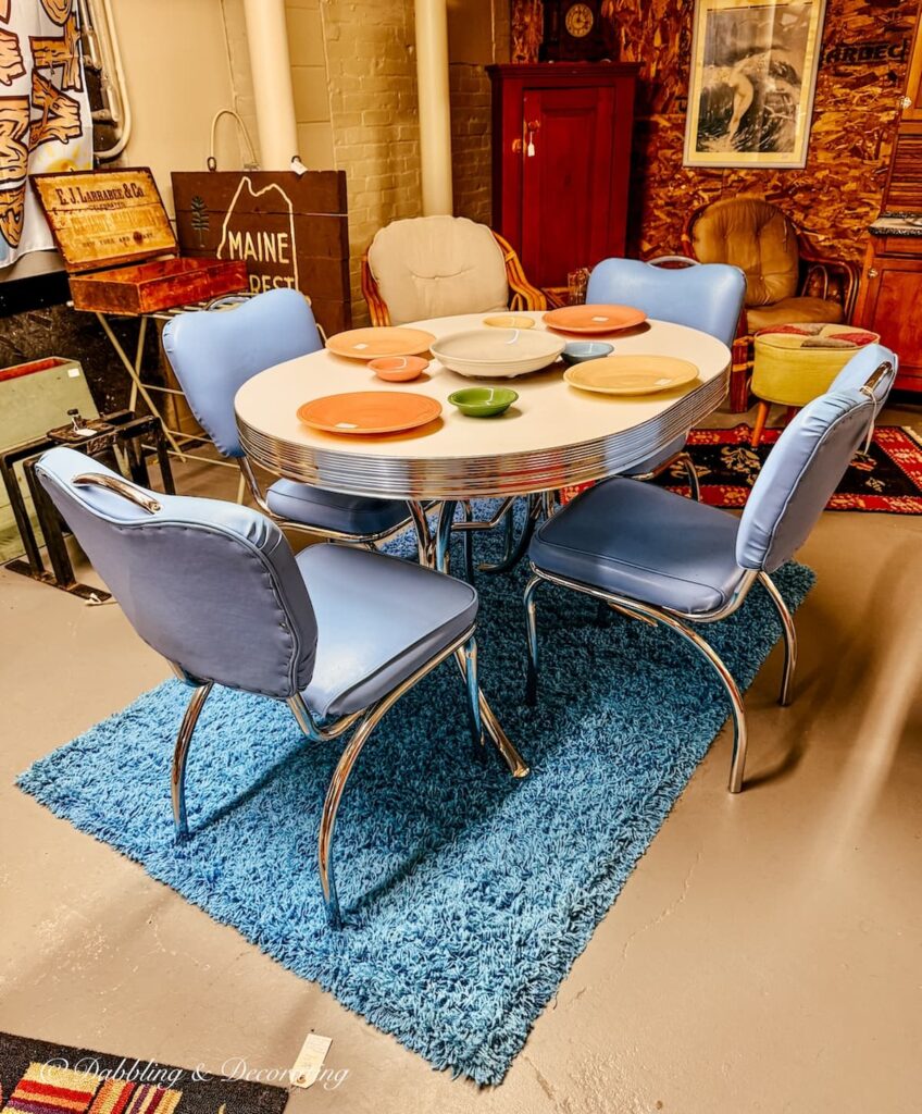 Retro kitchen table with blue chairs, a blue rug and colorful collection of 1950s plates displayed at Portland Antique Mall in Maine.