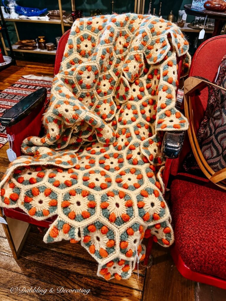 Orange and turquoise crochet blanket on red mid century modern chair in vintage urban decor.