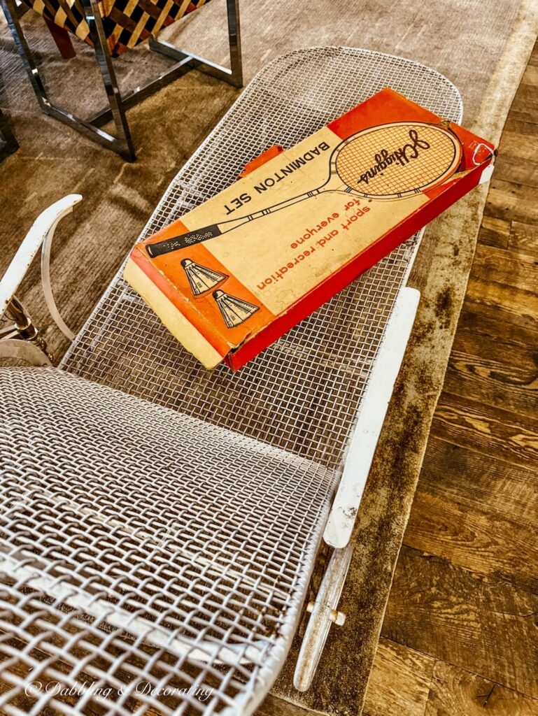 Old fashioned badminton set in retro box on white lounge chair in vintage retro wrought iron white chaise lounge.