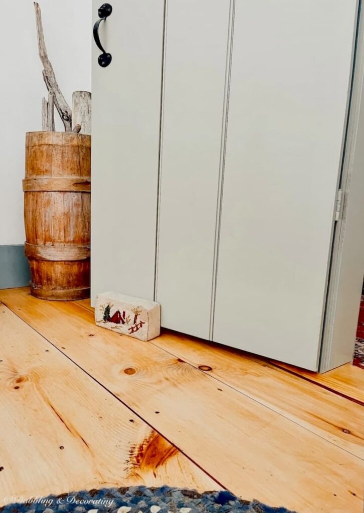 Vintage wooden barrel filled with beach driftwood next to open latched door in bedroom with soft pine wood flooring.